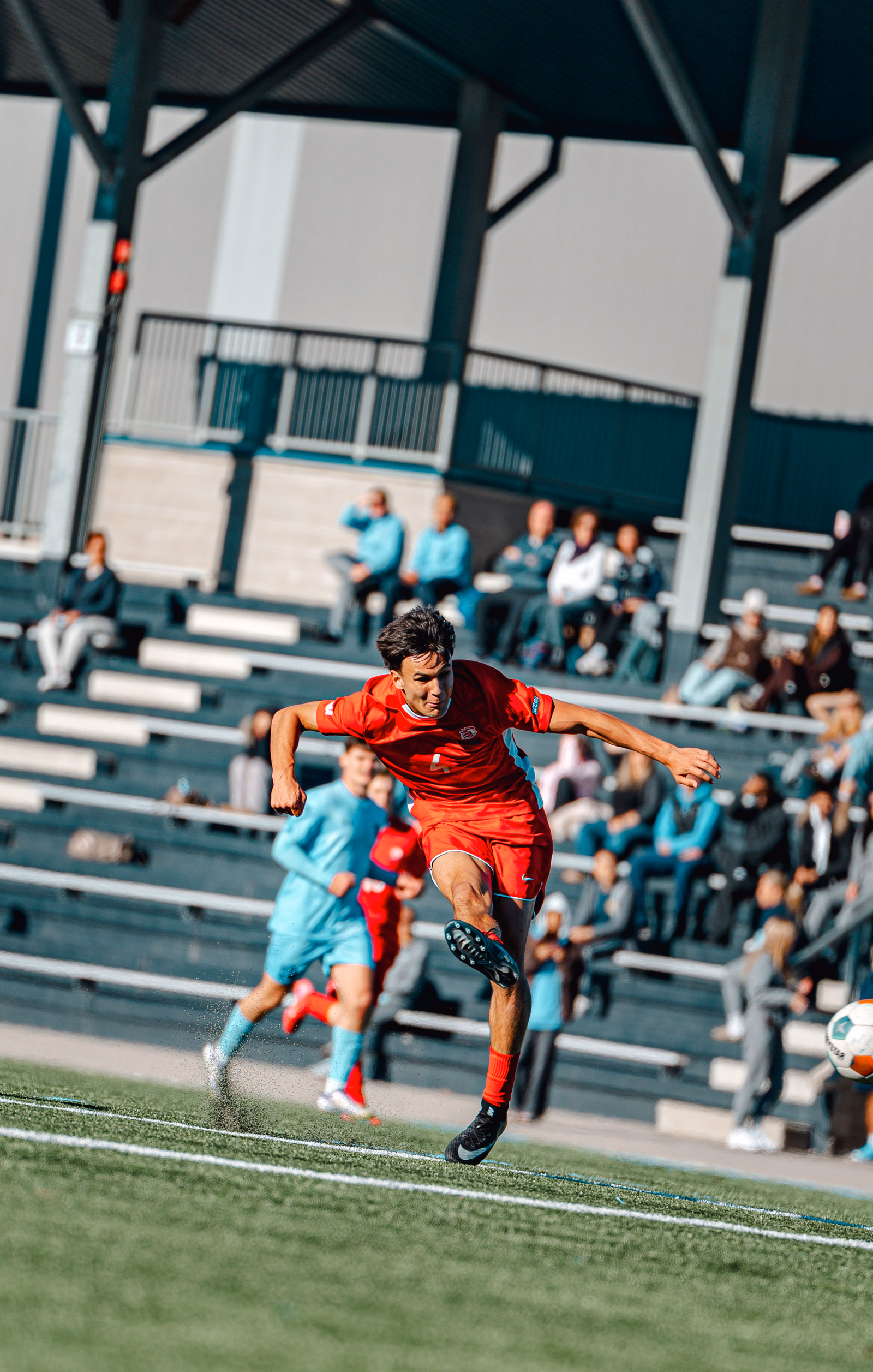 Football player in red following through on a kick in front of the stands