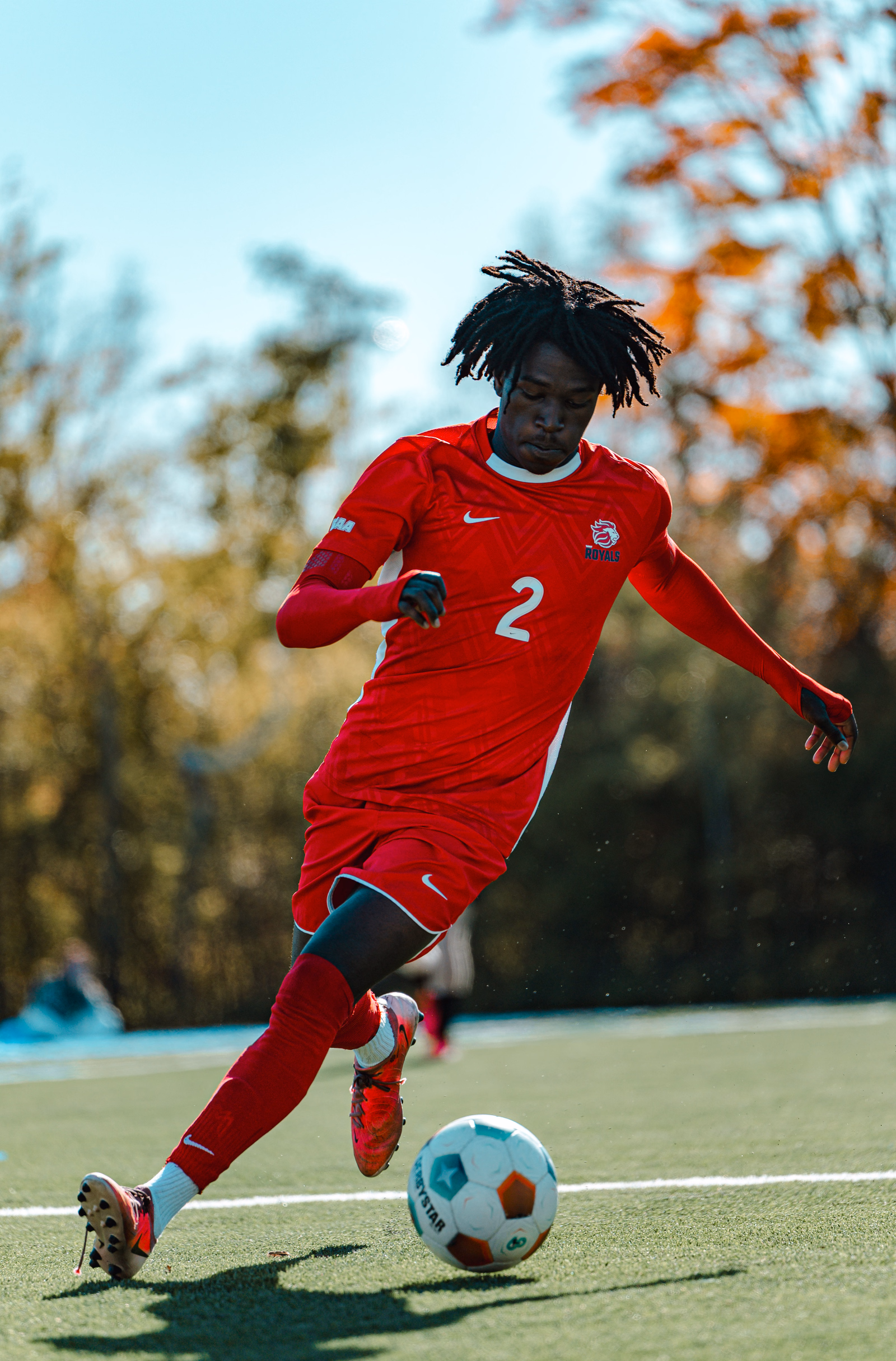 Football player in a red number 2 jersey striking the ball on an autumn afternoon