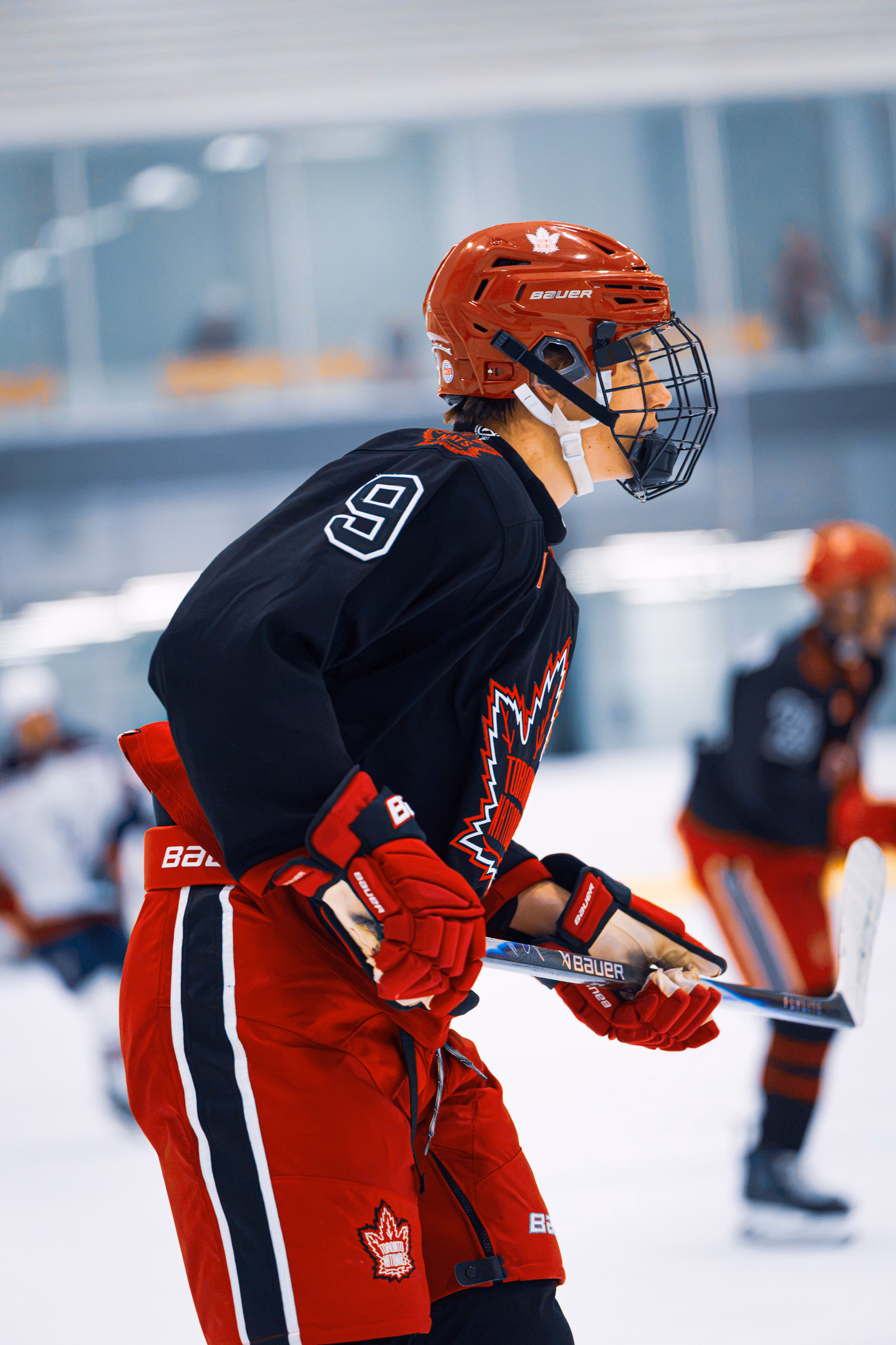 Hockey player wearing a red helmet and black number 9 jersey waiting on the ice