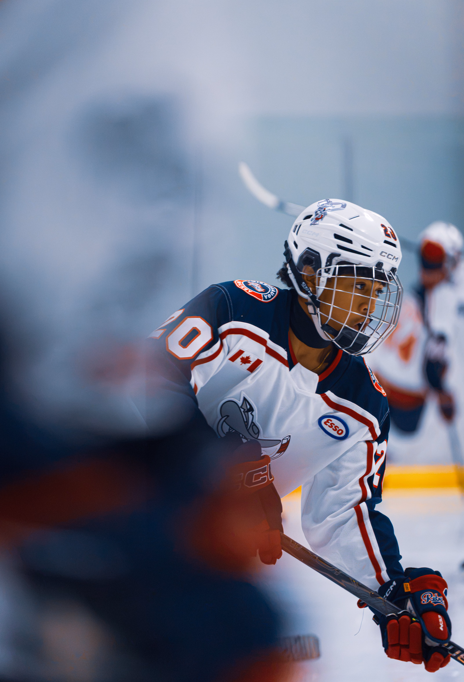 Rebels AAA number 20 leaning forward on the ice with a teammate blurred in the foreground